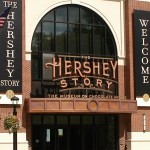 2-story red brick building with light stone accents , and larged arched glass window with the words Hershey Story Museum in chocolate brown letters.